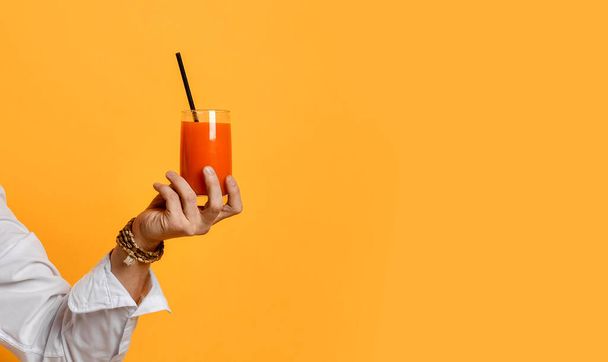 Mans hand holding glass of freshly squeezed juice or homemade fruit smoothie cocktail over yellow background - Photo, Image