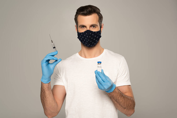 Masque de sécurité pour homme et gants en latex tenant un pot de vaccin et une seringue isolés sur du gris
  - Photo, image
