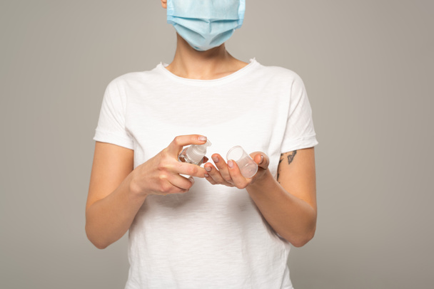 Vista ritagliata della donna in maschera medica utilizzando disinfettante per le mani isolato su grigio
  - Foto, immagini