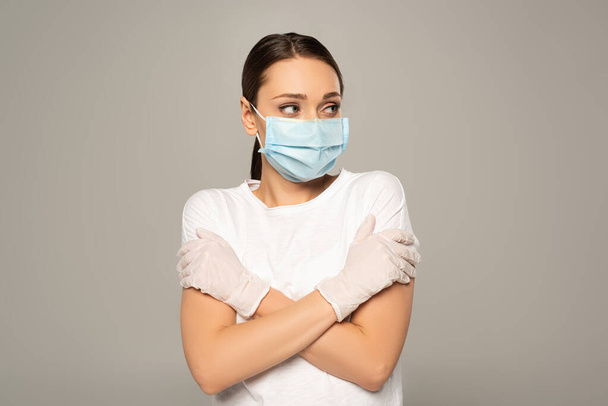 Молодая женщина в медицинской маске и латексных перчатках смотрит в сторону изолированной на сером
  - Фото, изображение