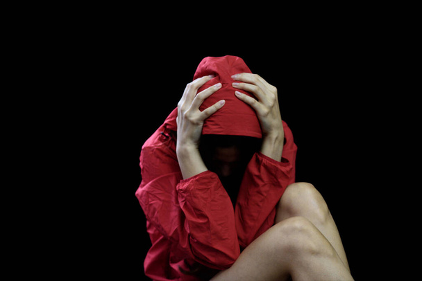 Femme asiatique qui porte un manteau rouge avec les mains sur la tête sur fond noir, concept de violence (discret
) - Photo, image