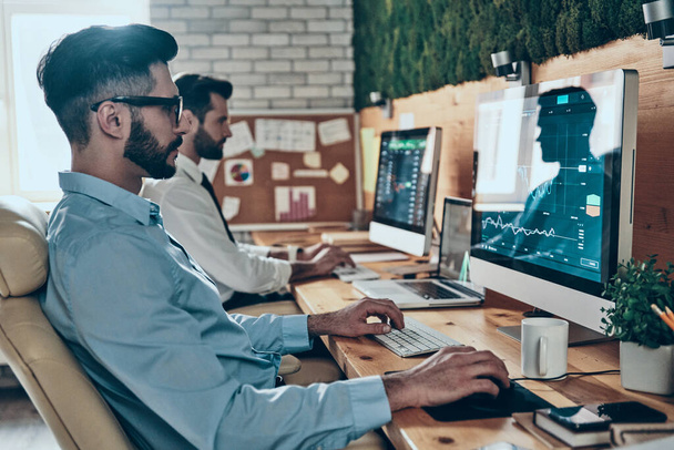 Два сконцентрированных молодых современных человека в формальной одежде работают за компьютерами, сидя в офисе
 - Фото, изображение