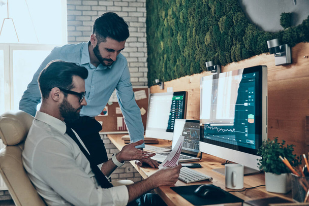 Resmi olarak iki yakışıklı genç adam ofiste otururken bilgisayar kullanarak çalışıyorlar. - Fotoğraf, Görsel