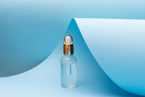 butelka olejku kosmetycznego z pipetą stojącą na niebieskim tle. koncepcja pielęgnacji skóry. Naturalny kosmetyk. Nowoczesny trend urody - Zdjęcie, obraz