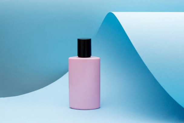 Perfumy stojące na niebieskim papierze. różowa butelka, Nowoczesny trend urody - Zdjęcie, obraz