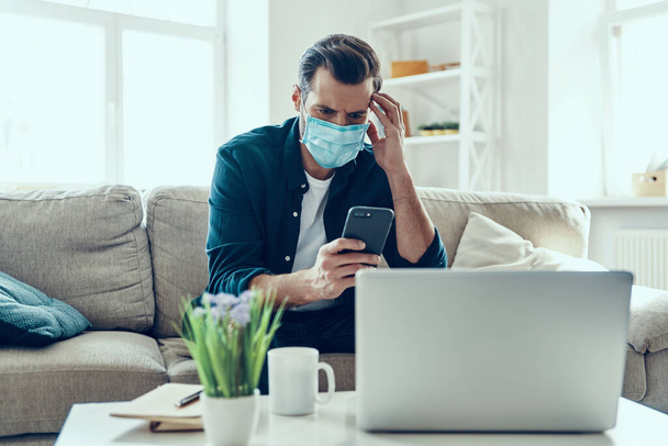 Young man in protective face mask using smartphone while working from home - Valokuva, kuva