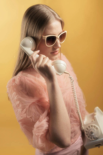 Rétro années 1960 femme de mode d'été en pull rose et lunettes de soleil appelant avec téléphone blanc
. - Photo, image