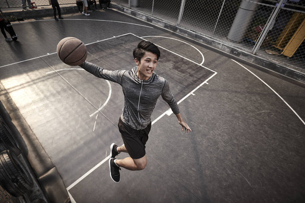 fiatal ázsiai felnőtt férfi kosárlabda játékos próbál slam zsákolás a szabadtéri pályán - Fotó, kép