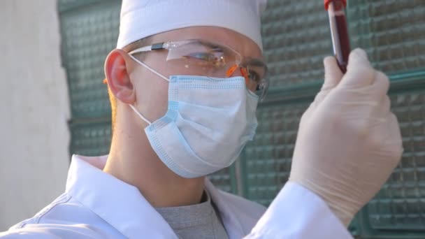 Doctor exploring test tube with blood sample to coronavirus. Medic with protective gloves and glasses viewing and testing blood analysis to COVID-19. Concept of health and safety life from pandemic - Materiaali, video