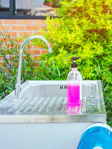 Ροζ μπουκάλι αλκοόλ τζελ ή αντιβακτηριακό σαπούνι απολυμαντικό σε νεροχύτες αλουμινίου στον κήπο, αλκοόλ τζελ για τον καθαρισμό του χεριού για την πρόληψη της εξάπλωσης των μικροβίων και των βακτηρίων και την αποφυγή λοιμώξεων του ιού του στέμματος (covid-19) - Φωτογραφία, εικόνα