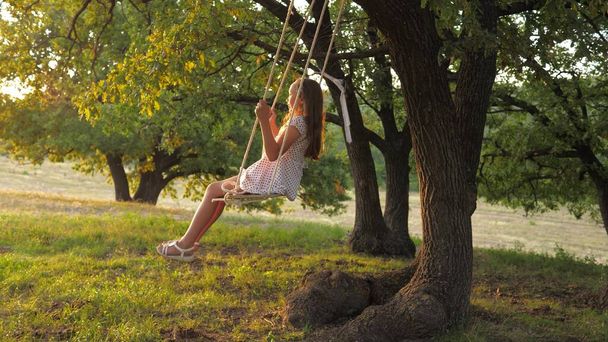 健康的な赤ちゃんの男の子。少女は木の上の公園でブランコに乗って遊んでいます。空を飛ぶ夢。幸せな家族と子供時代の概念。娘は公園で遊ぶ. - 写真・画像