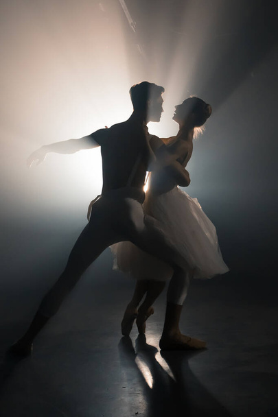 Professional ballet couple dancing in spotlights smoke on big stage. Beautiful young woman and man on floodlights background. Emotional duet performing choreographic art. - Foto, imagen