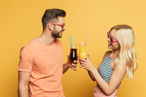 smiling young couple in sunglasses clinking cocktail glasses on yellow background - Foto, Imagem
