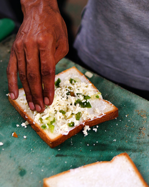 View of Indian street food vendor adding ingredients to bread slices to prepare Sandwich - Foto, Imagem