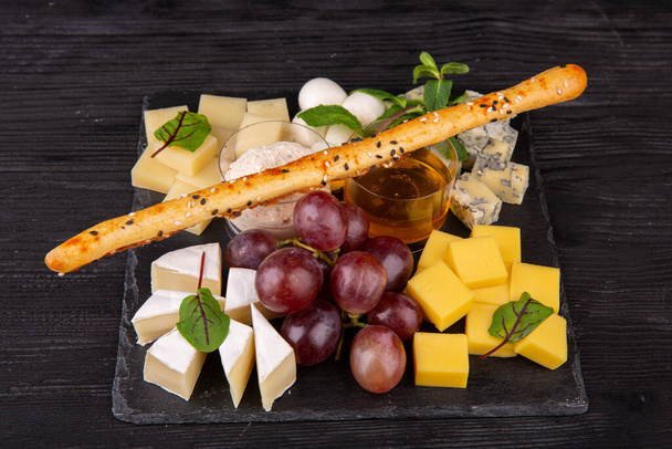 Cheese plate with different cheese varieties, served with honey and cream sauce with red grapes and mint - Фото, зображення