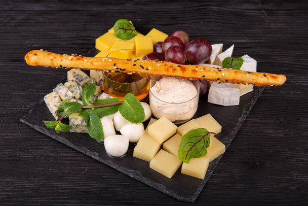 Cheese plate with different cheese varieties, served with honey and cream sauce with red grapes and mint - Photo, image