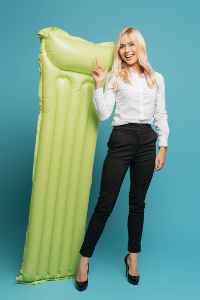 vista completa de la mujer de negocios sonriente que señala con el dedo en el colchón inflable sobre fondo azul
 - Foto, Imagen