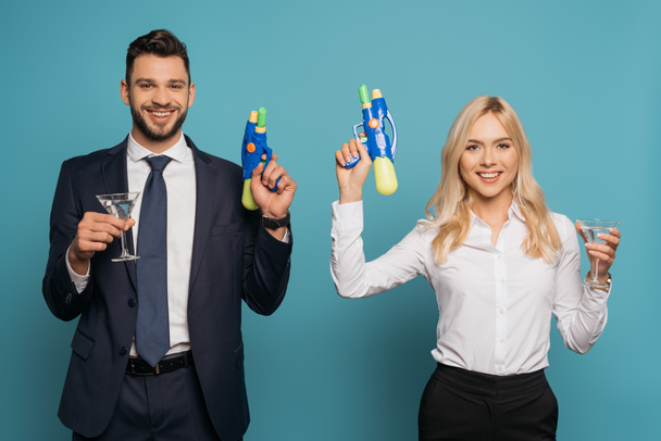 empresarios felices sosteniendo vasos de cóctel y pistolas de agua de juguete sobre fondo azul
 - Foto, imagen