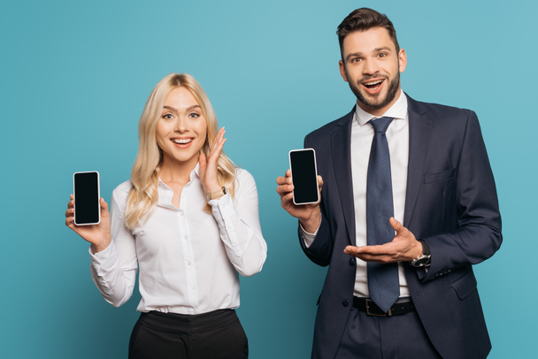 smiling businessman and businesswoman showing smartphones with blank screen on blue background - Foto, afbeelding