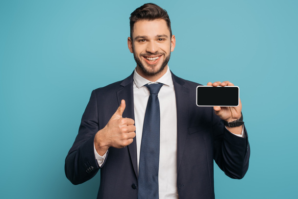 homem de negócios sorrindo mostrando polegar para cima enquanto segurando smartphone com tela em branco no fundo azul
 - Foto, Imagem