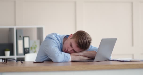 Unavený mladý muž spí na notebooku na pracovišti - Záběry, video