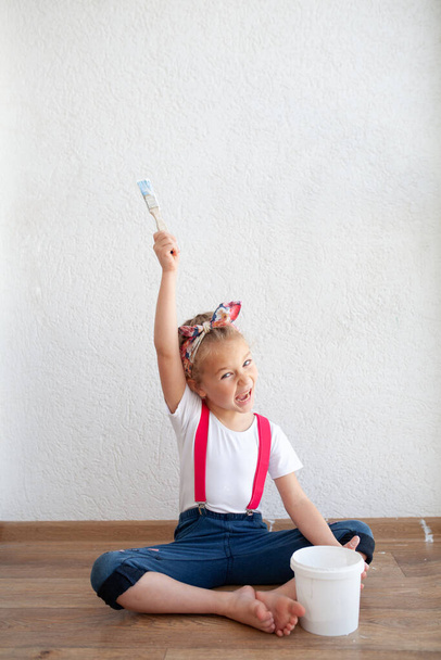 Little pretty fun girl paints a white wall with a brush, a child and repairs in the apartment, indoor - Foto, Imagen
