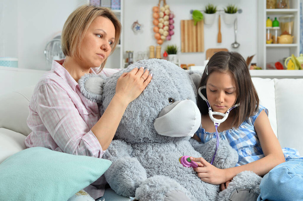  little girl and mother playing   with toy teddy  bear in facial mask. Girl with stethoscope - Фото, зображення
