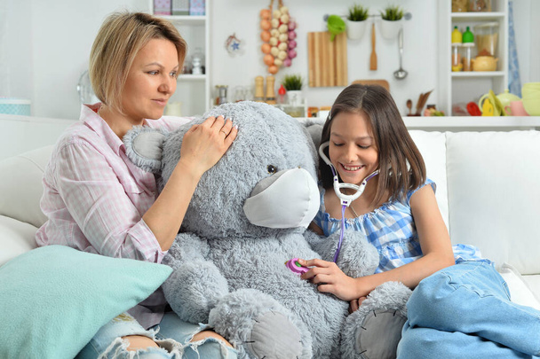  little girl and mother playing   with toy teddy  bear in facial mask. Girl with stethoscope - Fotó, kép