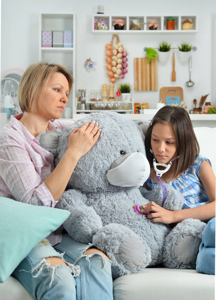  little girl and mother playing   with toy teddy  bear in facial mask. Girl with stethoscope - Photo, Image