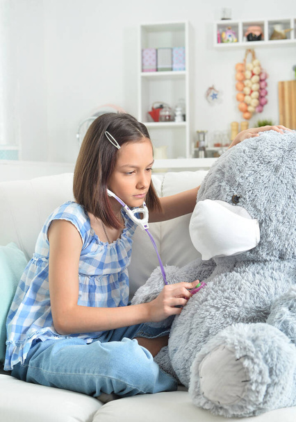  little girl  with stethoscope playing with  toy teddy  bear in facial mask - Foto, Imagen