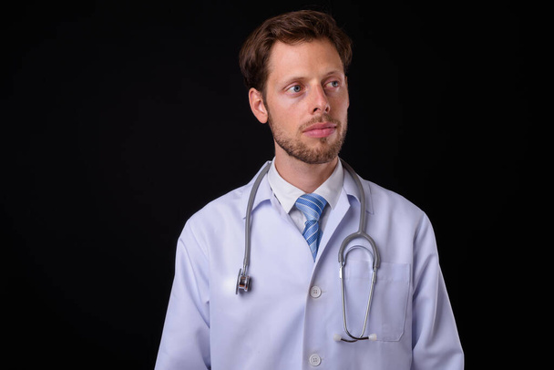 Studioaufnahme eines gutaussehenden bärtigen Arztes vor schwarzem Hintergrund - Foto, Bild