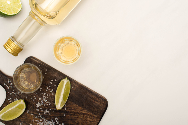 top view of golden tequila with lime, salt on wooden cutting board on white marble surface - Foto, immagini