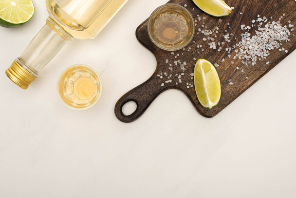 top view of golden tequila with lime, salt on wooden cutting board on white marble surface - Фото, зображення