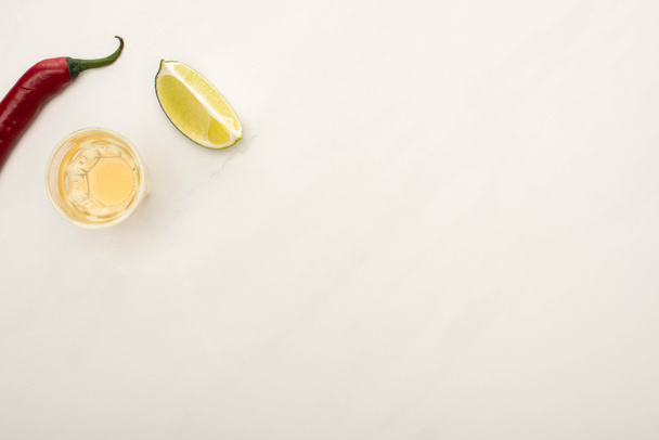 top view of golden tequila with lime, chili pepper on white marble surface - Photo, Image