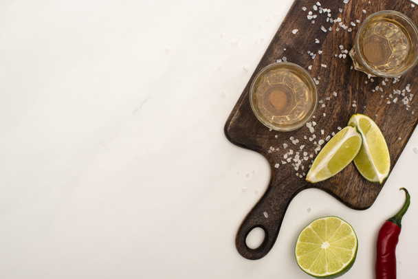 vista dall'alto di tequila dorata con lime, peperoncino, sale su tagliere in legno su superficie di marmo bianco
 - Foto, immagini