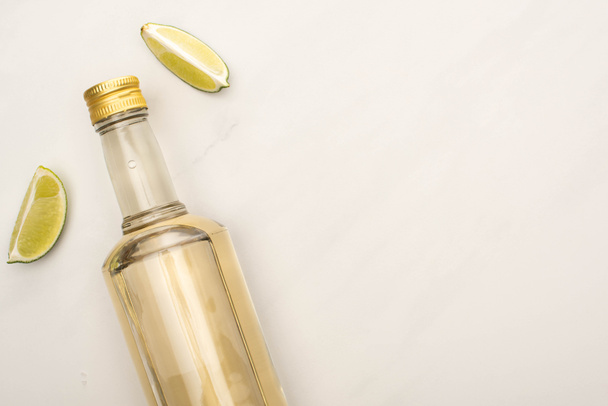 top view of golden tequila in bottle with lime on white marble surface - Foto, afbeelding