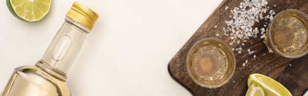 vista superior de tequila dorado con cal, sal sobre tabla de cortar de madera sobre superficie de mármol blanco, plano panorámico
 - Foto, Imagen