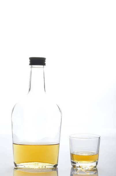 Glass transparent bottle with strong alcohol. Next to a glass of alcohol. On a white background. - Valokuva, kuva