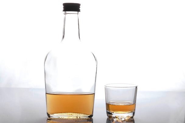 Glass transparent bottle with strong alcohol. Next to a glass of alcohol. On a white background. - Foto, Bild