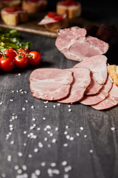 selective focus of tasty ham sliced ham, cherry tomatoes, parsley, salt on wooden grey table - Photo, Image