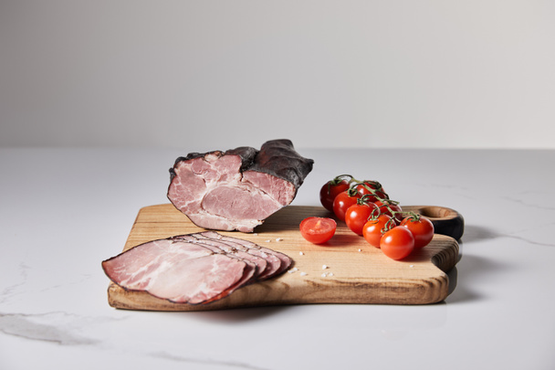 tasty ham on cutting board with salt and cherry tomatoes on white marble surface isolated on grey - 写真・画像