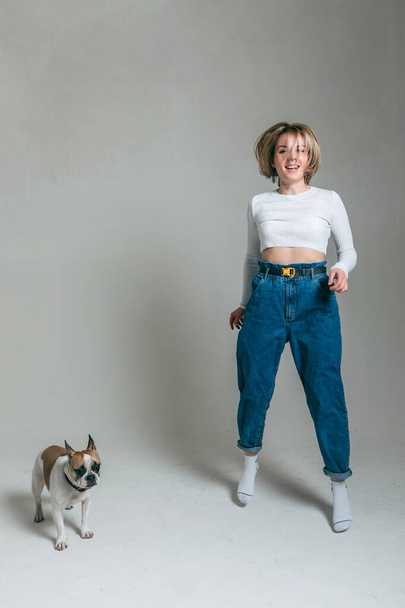 een jong meisje speelt met haar grappig frans bulldog in de studio met een witte achtergrond - Foto, afbeelding