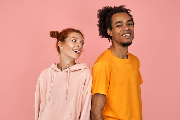 Delighted handsome black male and ginger female rejoice successfully passed exam, look happily at each other, laugh at good joke, express positive emotions, isolated over pink background - Photo, image