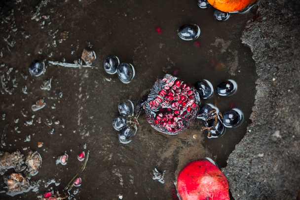 Rotten pomegranates and grapes in the puddle. Spoilt products. - Fotografie, Obrázek