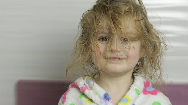 Pikkutyttö, jolla on märät hiukset kylpytakissa, irvistelee. Hymyä uimisen jälkeen
 - Valokuva, kuva