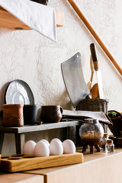 selective focus of clay mugs near sharp knifes, cotton napkins and raw eggs  - Photo, Image