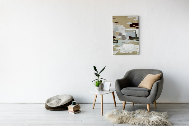 cómodo sillón cerca de la mesa de centro con plantas verdes, marco y pintura en la pared en la sala de estar moderna
  - Foto, Imagen