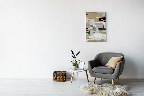 現代のリビングルームに緑の植物やフレームとコーヒーテーブルの近くの快適なグレーのアームチェア  - 写真・画像