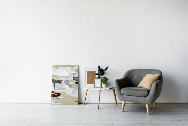 párna szürke fotel mellett dohányzóasztal zöld növények és keretek a modern nappaliban  - Fotó, kép