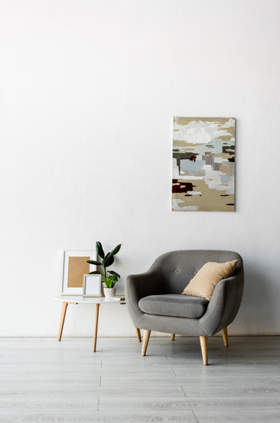 szürke fotel közelében dohányzóasztal keretekkel és zöld növények közelében festmény a falon a modern nappaliban  - Fotó, kép